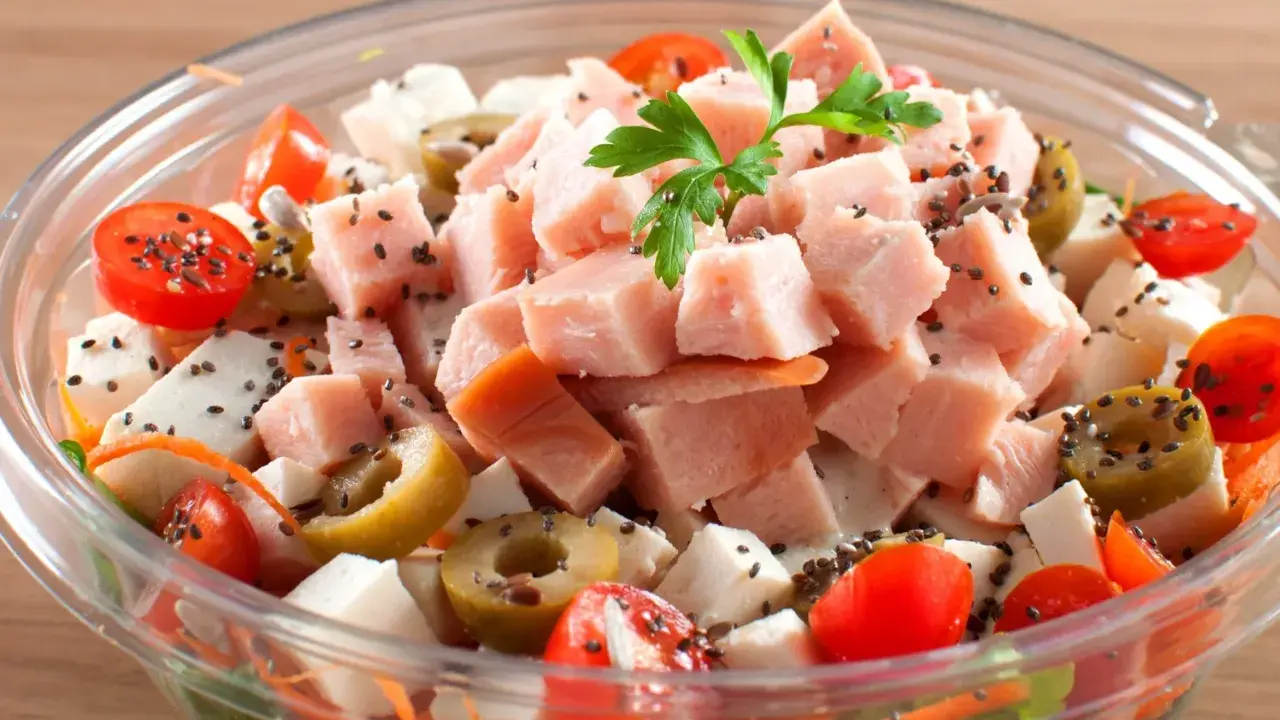 Pyszna sałatka z wędzonym kurczakiem, pomidorkami koktajlowymi, oliwkami i serem feta, posypana czarnuszką.