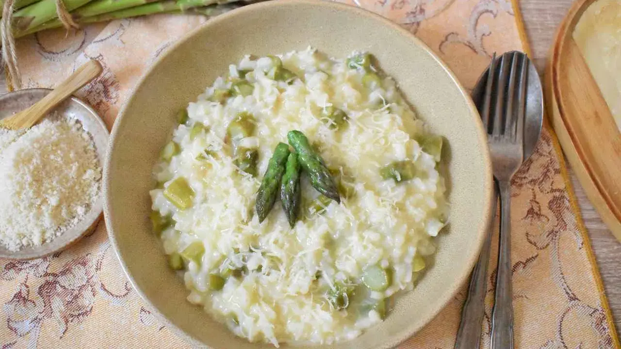 Kremowe risotto ze szparagami, posypane parmezanem, z kilkoma zielonymi szparagami na wierzchu.