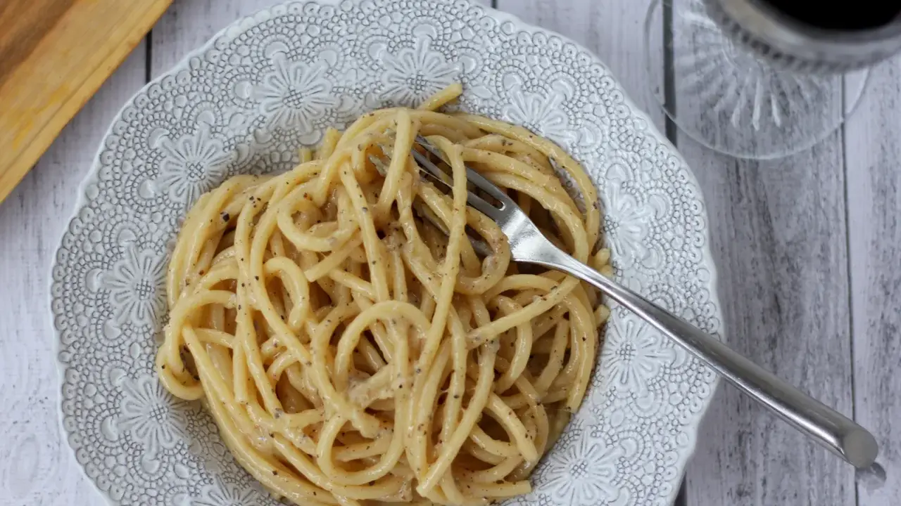 Porcja pysznego cacio e pepe z widelcem w talerzu, gotowa do zjedzenia.