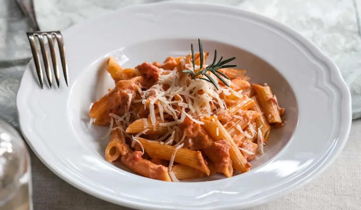 Penne alla vodka z kremowym sosem pomidorowym, posypane parmezanem i udekorowane gałązką rozmarynu.