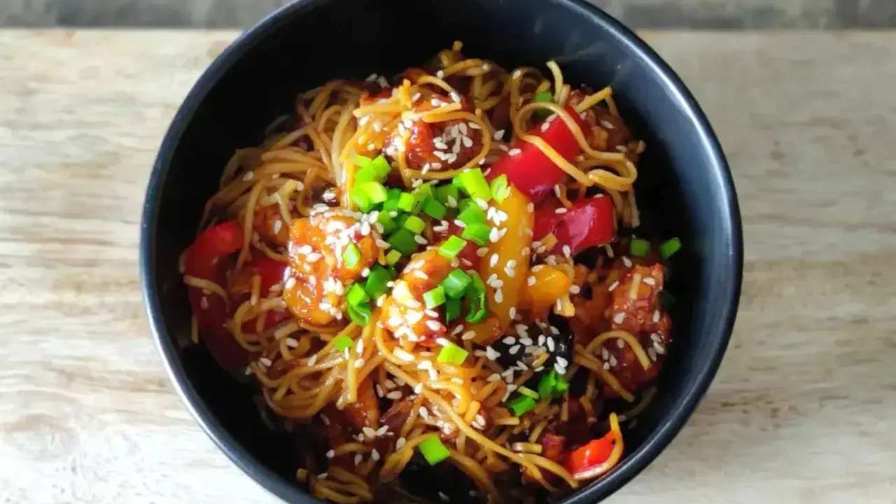 Pyszny makaron chow mein z kurczakiem, papryką i szczypiorkiem, posypany sezamem.