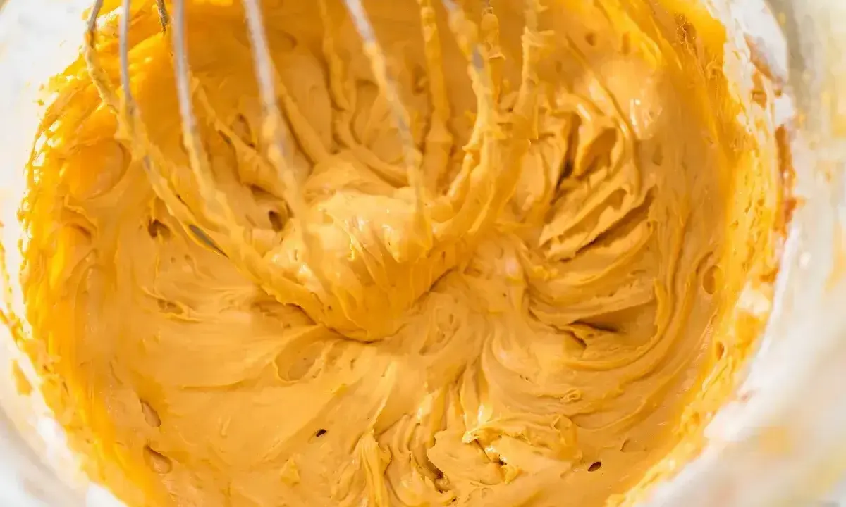 Mieszanie puszystego, złocistego kremu do tortu z mascarpone za pomocą trzepaczki miksera.