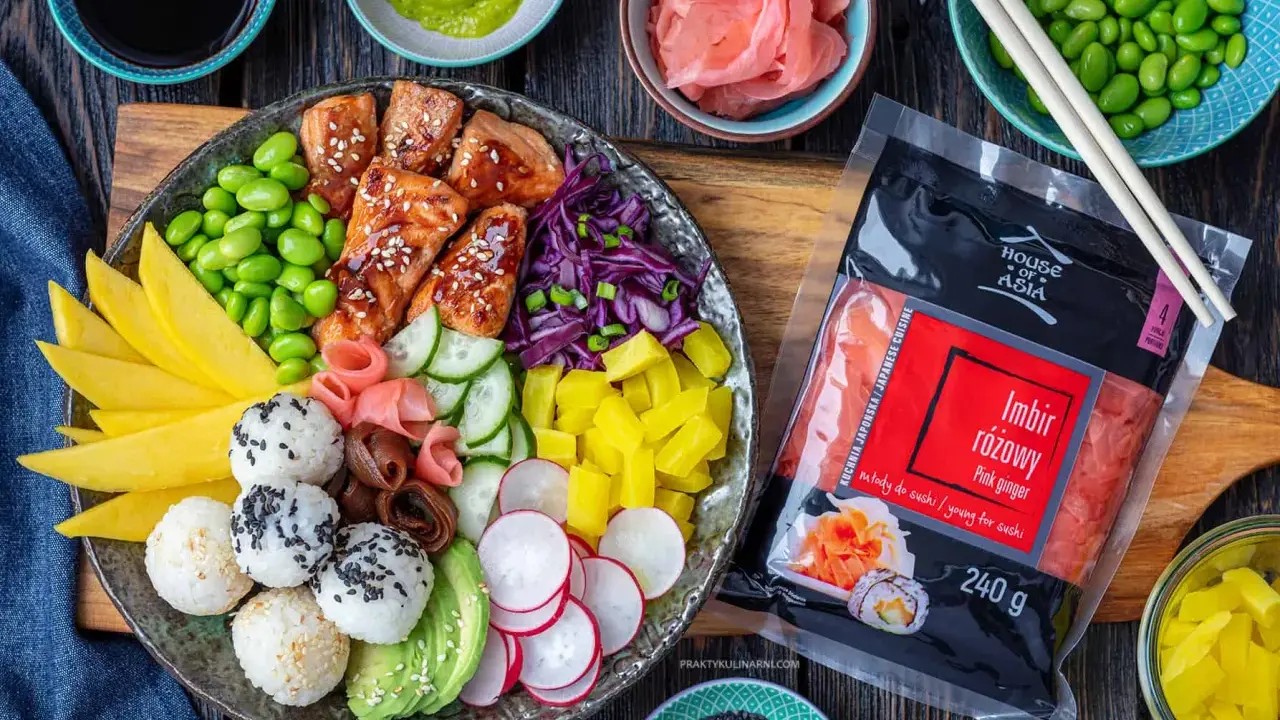 Kolorowy bowl z lososiem, ryżowymi kulkami, mango, awokado, edamame i marynowanym imbirem. Obok opakowanie różowego imbiru.