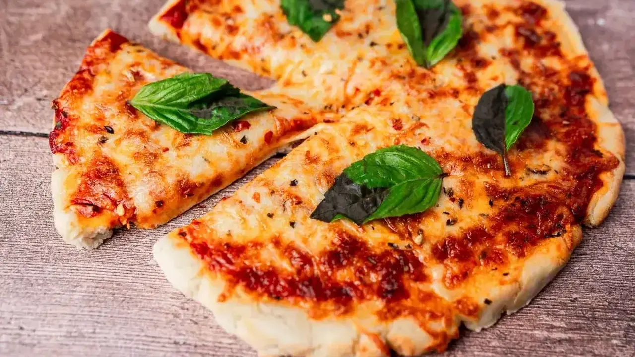 Pyszna pizza z air fryera, z ciągnącym się serem i świeżą bazylią, wygląda apetycznie na drewnianym blacie.