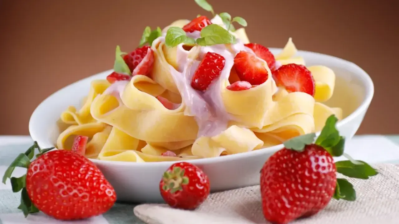 Pappardelle z kremowym sosem i świeżymi truskawkami, ozdobione listkami mięty. Letnia uczta z makaronem i truskawkami.