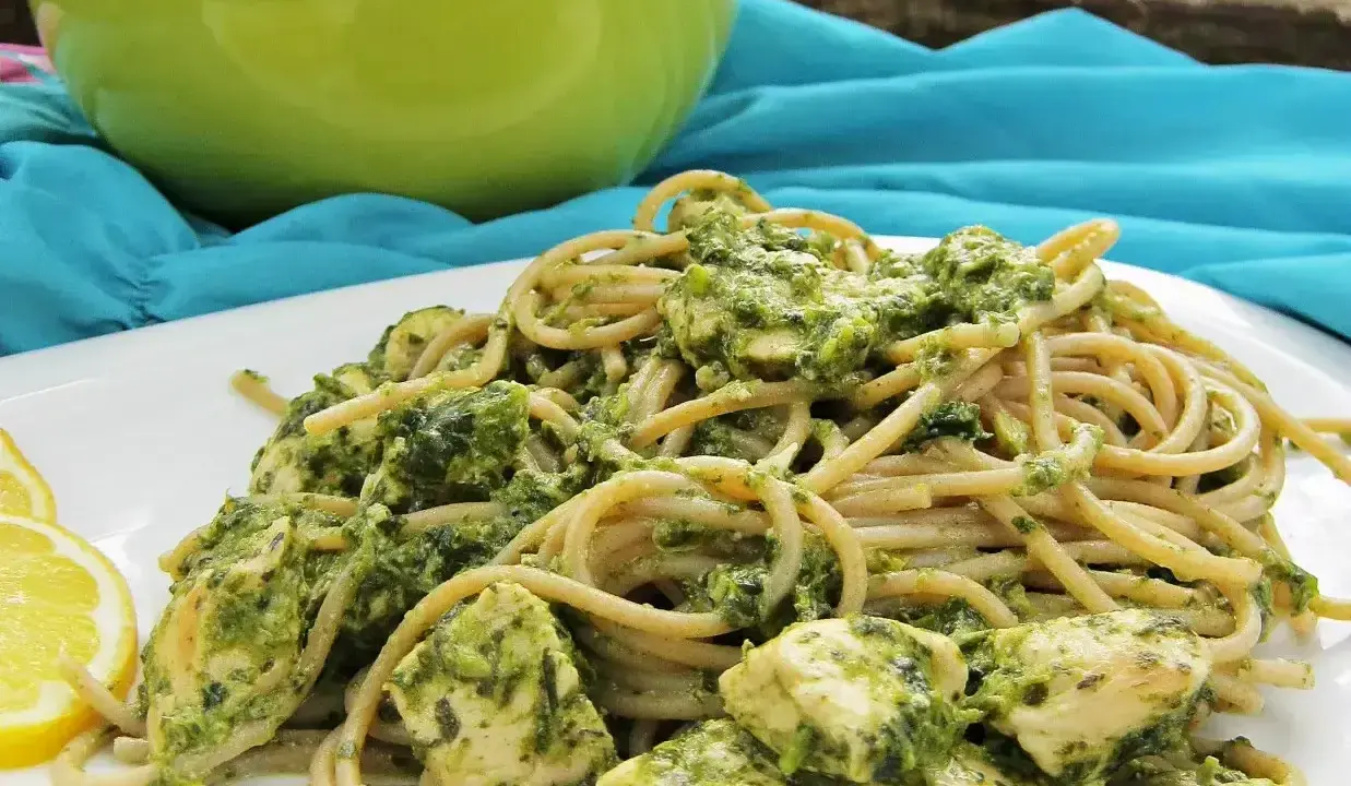 Pyszny makaron z pesto i kurczakiem, podany z plasterkami cytryny.