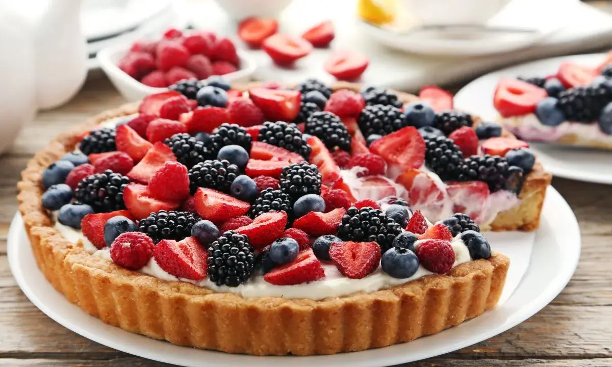 Pyszna tarta z mascarpone, udekorowana malinami, jeżynami i borówkami.