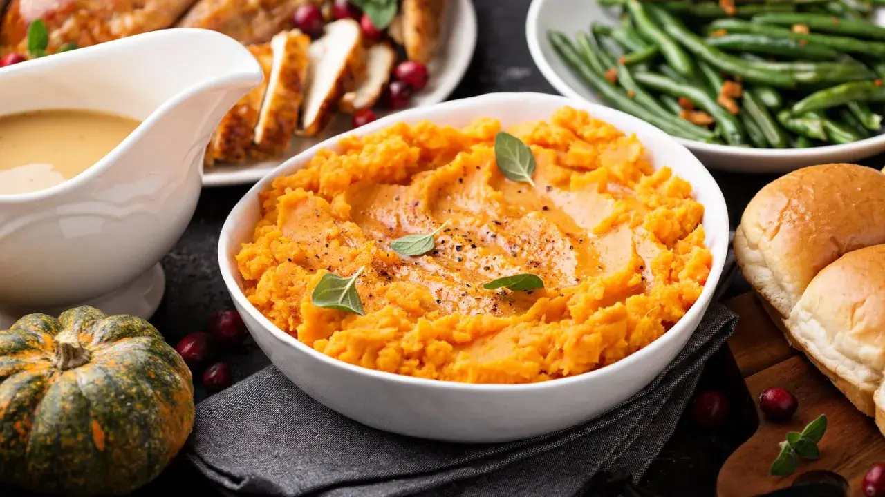 Aksamitne puree z batata, ozdobione listkami ziół, stanowi centralny punkt świątecznego stołu. Obok pieczony indyk, fasolka szparagowa i bułeczki.