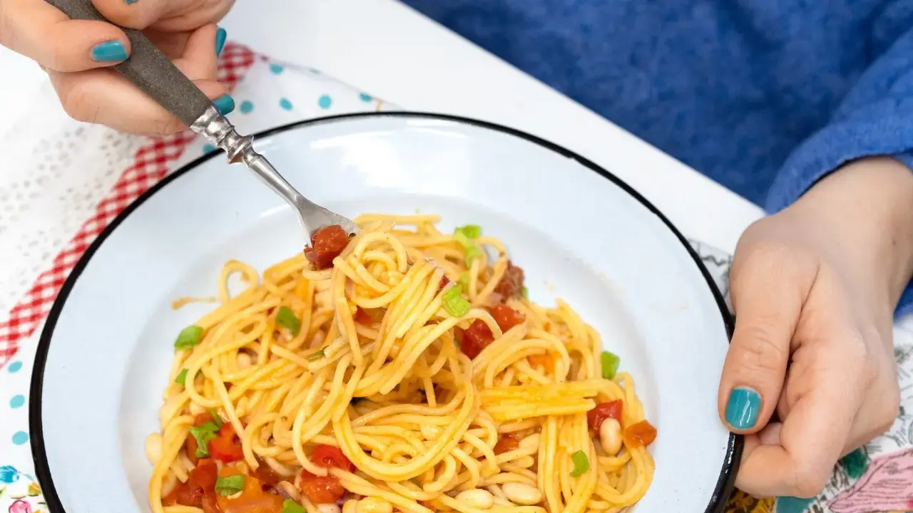 Pyszny obiad bez mięsa: spaghetti z pomidorami, fasolką i szczypiorkiem na talerzu.