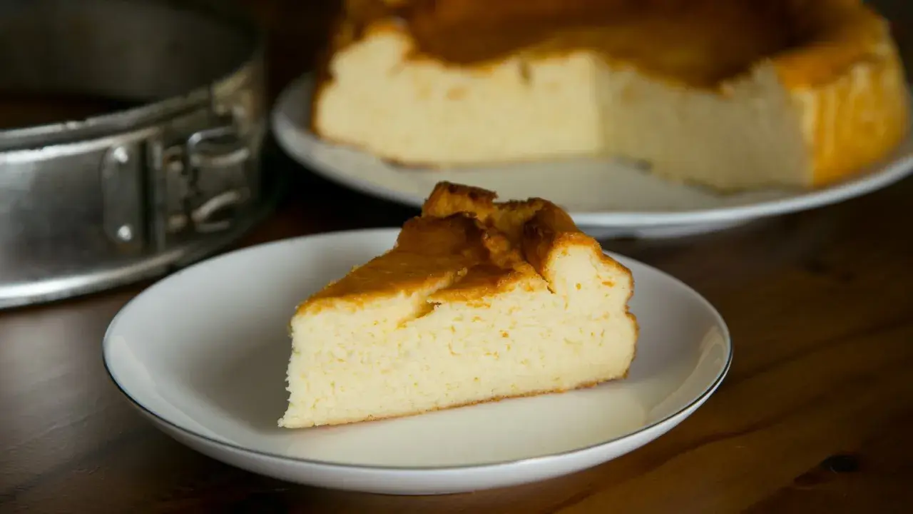 Puszysty sernik z mlekiem skondensowanym, z lekko zarumienioną skórką, na talerzyku. Obok forma do pieczenia.