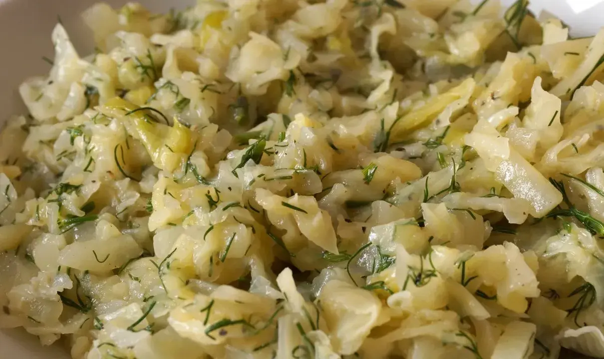Młoda kapusta zasmażana z koperkiem, podana w białej misce. Danie wygląda na delikatne i aromatyczne.