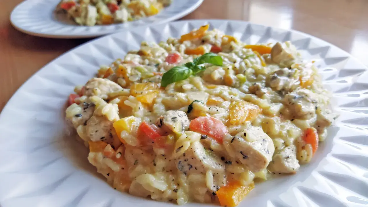 Pyszne risotto z kurczakiem i kolorowymi warzywami, udekorowane listkiem bazylii. Idealne na obiad.