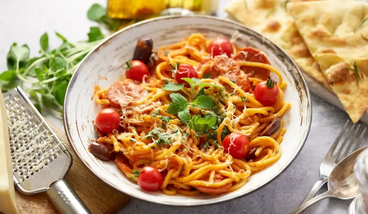 Pyszny makaron z chorizo, pomidorkami koktajlowymi i świeżą bazylią, posypany parmezanem. Idealny na szybki obiad.