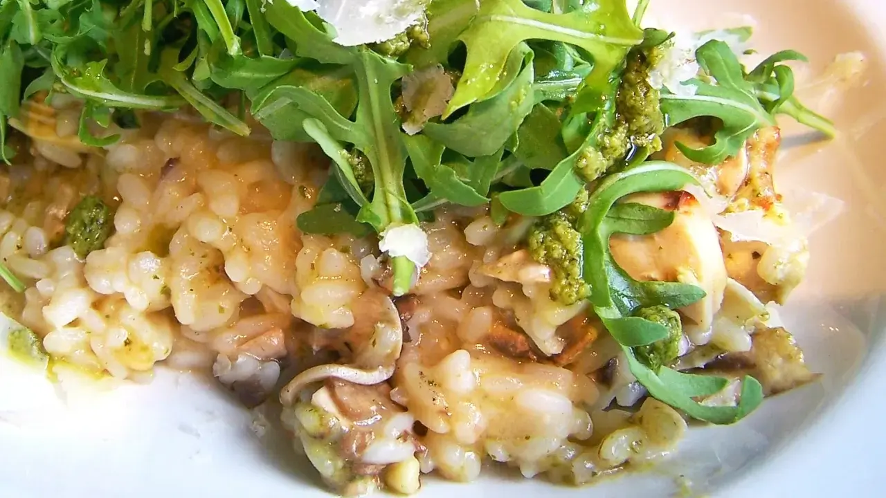 Kremowe risotto z pieczarkami, polane zielonym pesto i posypane parmezanem, udekorowane świeżą rukolą.