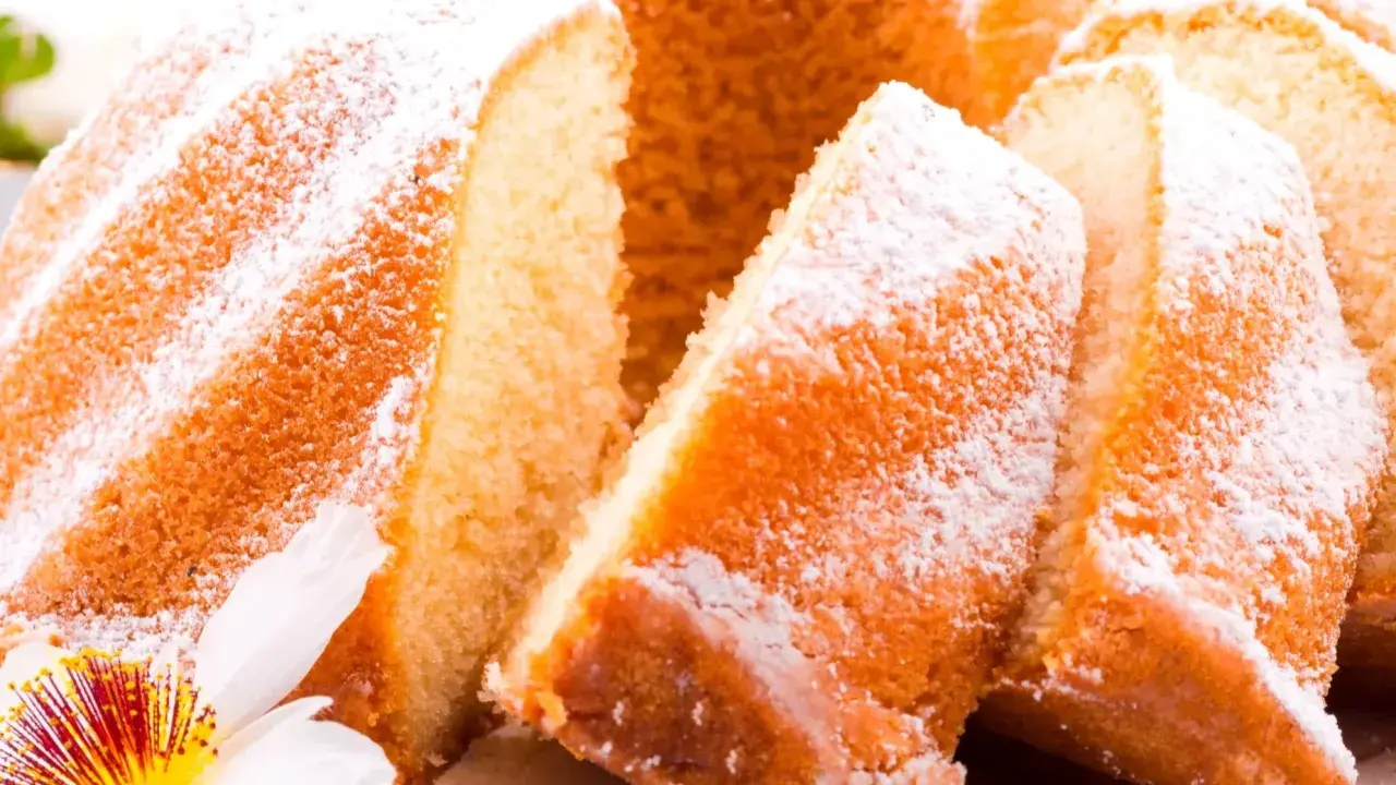 Szybka babka wilgotna, oprószona cukrem pudrem, z widocznymi kawałkami ciasta i ozdobiona kwiatem.