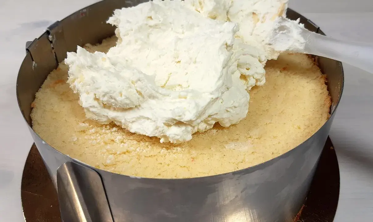 Nakładanie puszystego kremu z mascarpone na biszkopt w tortownicy.