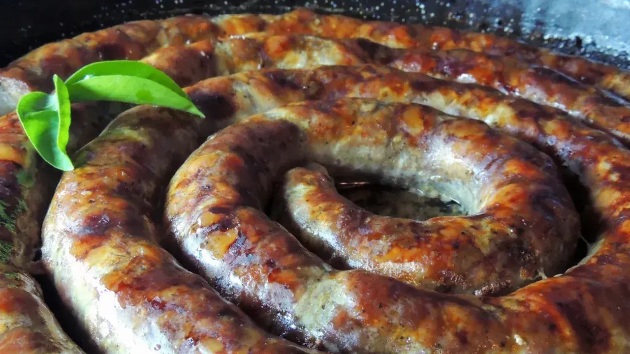 Złocista, pieczona biała kiełbasa w kształcie spirali, skropiona tłuszczem, z zielonym listkiem.