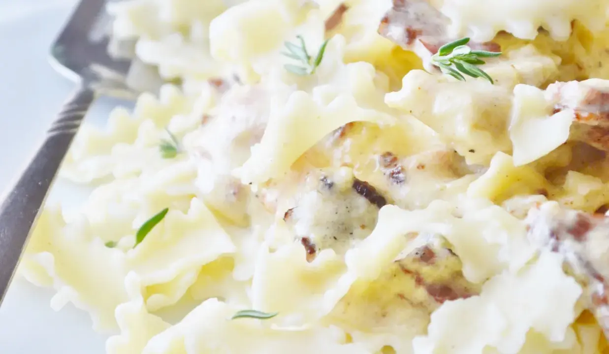 Pyszny makaron farfalle w kremowym sosie śmietanowym z kawałkami boczku i świeżym rozmarynem.