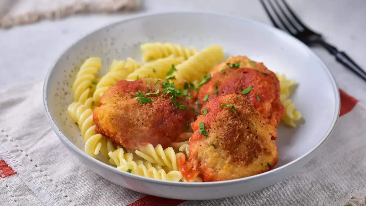 Elegancki obiad dla gości: pulpeciki w sosie pomidorowym z makaronem fusilli, posypane natką pietruszki.