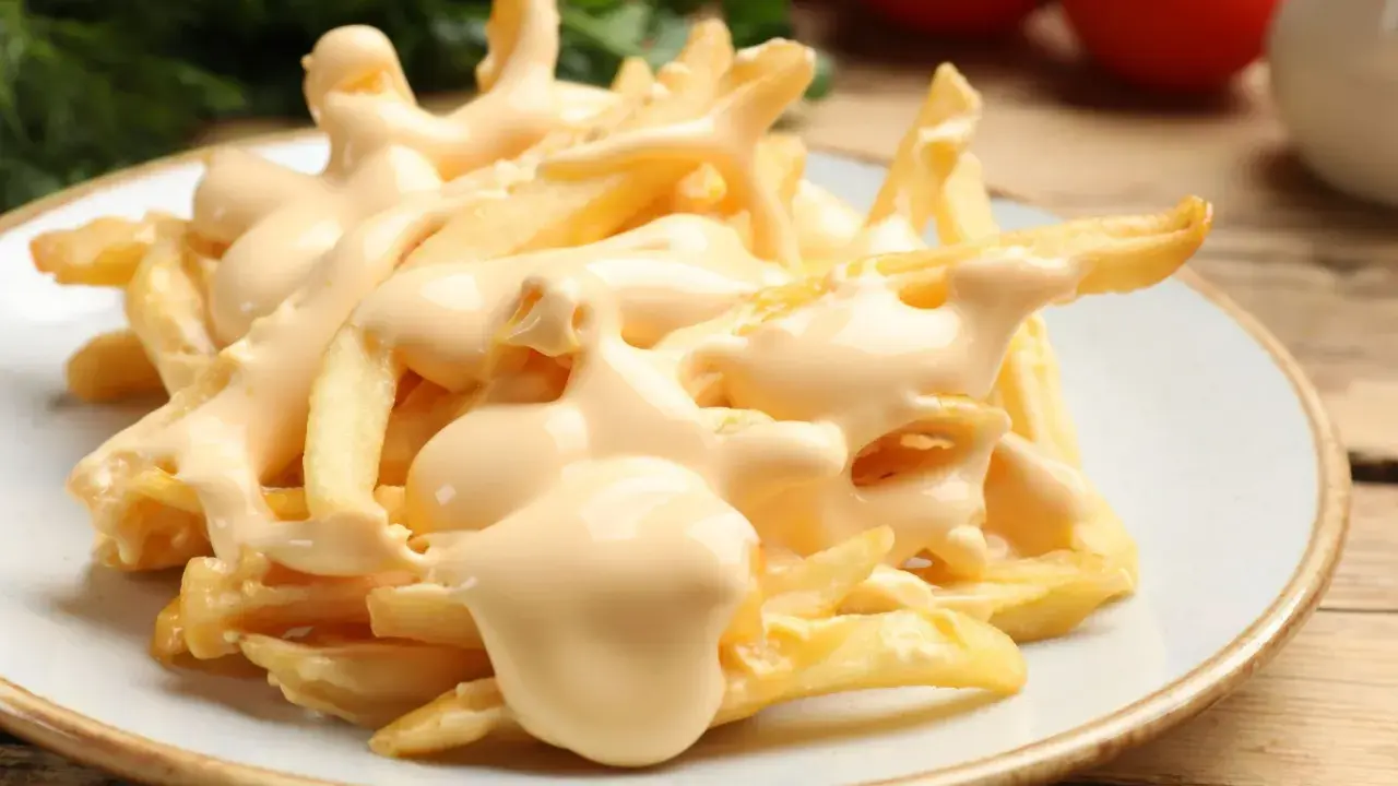 Chrupiące frytki z airfryer polane kremowym sosem serowym. Idealna przekąska, która rozpływa się w ustach.