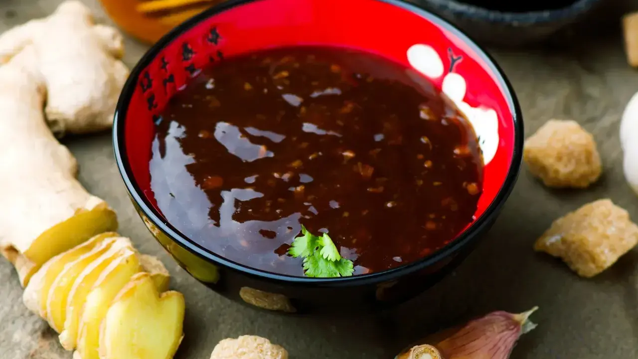 Miseczka z sosem teriyaki, obok świeży imbir, czosnek i cukier. Idealne składniki do przygotowania domowego sosu teriyaki.