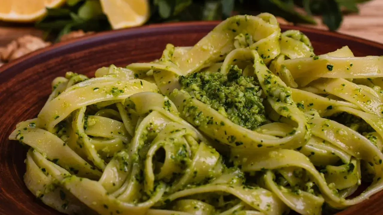 Tagliatelle z aromatycznym pesto z rukoli, podane na brązowym talerzu, z cytryną i orzechami w tle.