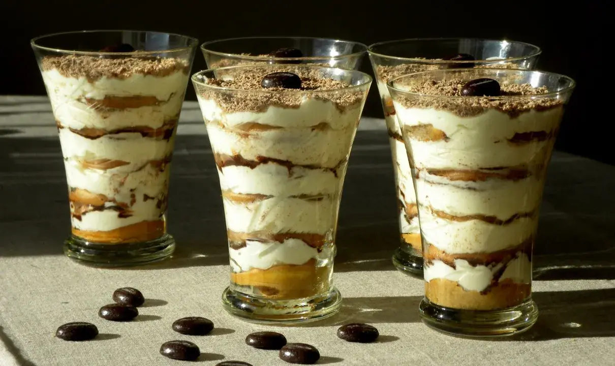 Pyszne tiramisu w pucharkach, warstwowo ułożone z kremem i biszkoptami, posypane czekoladą i kawą.