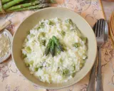 Kremowe risotto ze szparagami, posypane parmezanem, z kilkoma zielonymi szparagami na wierzchu.