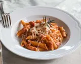 Penne alla vodka z kremowym sosem pomidorowym, posypane parmezanem i udekorowane gałązką rozmarynu.