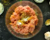 Mielone mięso na kebab z przyprawami w szklanej misce. Obok posiekana cebula, czosnek i łyżeczka z przyprawami.