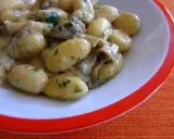 Pyszne gnocchi z sosem grzybowym i natką pietruszki, podane w białej misce z pomarańczowym rantem.