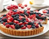 Pyszna tarta z mascarpone, udekorowana malinami, jeżynami i borówkami.