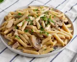 Penne z kurczakiem i pieczarkami w kremowym sosie, posypane natką pietruszki. Pyszne danie makaronowe.