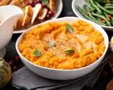 Aksamitne puree z batata, ozdobione listkami ziół, stanowi centralny punkt świątecznego stołu. Obok pieczony indyk, fasolka szparagowa i bułeczki.