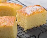 Puszyste ciasto z kaszy manny, pokrojone w kostkę, z posypką z cukru pudru, na czarnej kratce.