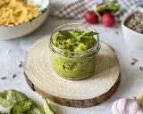 Pesto z liści rzodkiewki w słoiczku, ozdobione natką pietruszki. Obok makaron, rzodkiewki i czosnek.