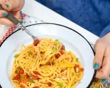Pyszny obiad bez mięsa: spaghetti z pomidorami, fasolką i szczypiorkiem na talerzu.