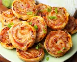 Pyszne pizzerinki z ciasta francuskiego, posypane sezamem i szczypiorkiem, ułożone na talerzu.
