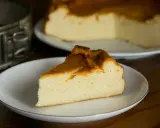 Puszysty sernik z mlekiem skondensowanym, z lekko zarumienioną skórką, na talerzyku. Obok forma do pieczenia.