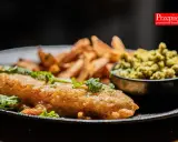 Chrupiący fish and chips z zielonym groszkiem i świeżą miętą na czarnym talerzu.