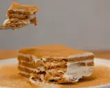 Pyszne ciasto na herbatnikach z kremem, kawałek na widelcu unosi się nad deserem.