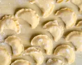 Surowe pierogi z farszem na pierogi ruskie, ułożone na drewnianym blacie, posypane mąką.