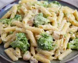 Penne z kurczakiem i kremowym sosem, w którym dominują zielone różyczki brokułów. Danie posypane startym parmezanem.