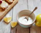 Gęsty, biały lukier do cynamonek w miseczce, obok cytryny i kawałków cytryny.