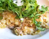 Kremowe risotto z pieczarkami, polane zielonym pesto i posypane parmezanem, udekorowane świeżą rukolą.