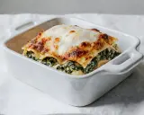 Pyszne lasagne ze szpinakiem, zapieczone pod złotą warstwą sera, w białej ceramicznej formie.