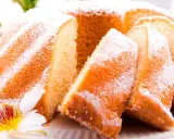Szybka babka wilgotna, oprószona cukrem pudrem, z widocznymi kawałkami ciasta i ozdobiona kwiatem.