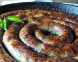 Złocista, pieczona biała kiełbasa w kształcie spirali, skropiona tłuszczem, z zielonym listkiem.