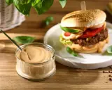 Pyszny sos do hamburgerów w słoiczku, obok soczystego burgera z dodatkami. Idealny do każdej kanapki.