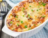 Pyszne, zapiekane mac and cheese w białym naczyniu, posypane szczypiorkiem i parmezanem. Obok widelce i luźne makarony.